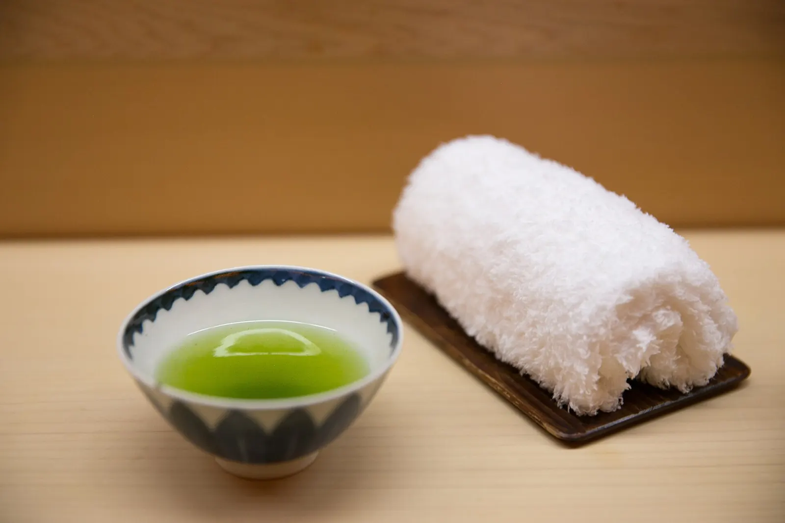 A rolled white Imabari towel next to a bowl of green tea