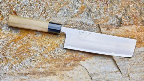 A Japanese nakiri knife with a wooden wa handle on a stone surface