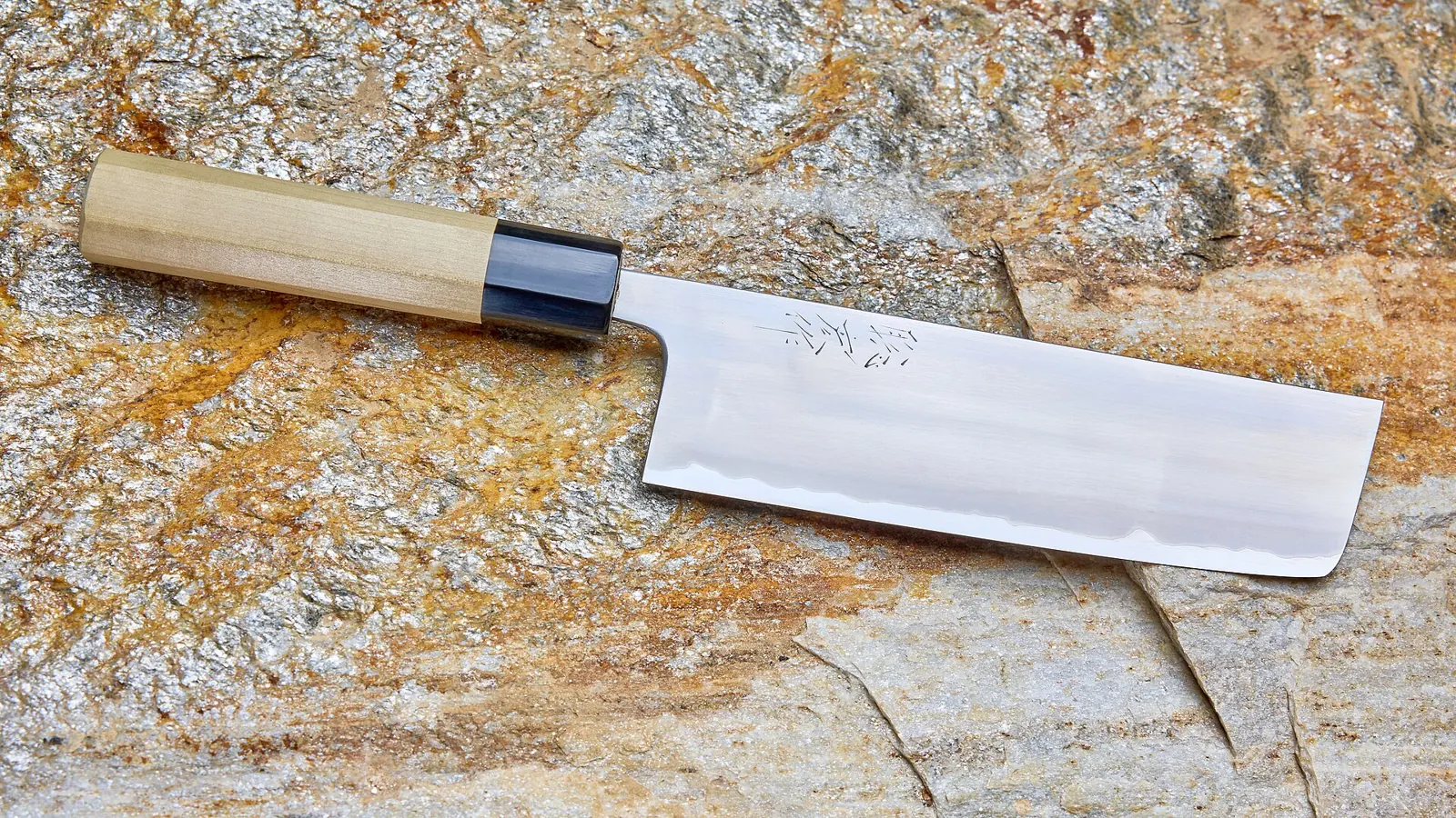 A Japanese nakiri knife with a wooden wa handle on a stone surface
